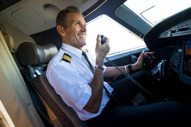 A mature White pilot holding the radio inside the cockpit of a private jet.